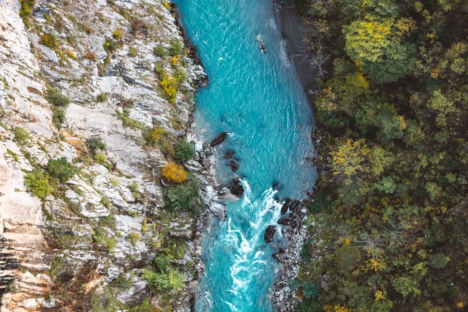 Drone captures a breathtaking view of a turquoise river flowing through a rugged forest landscape.