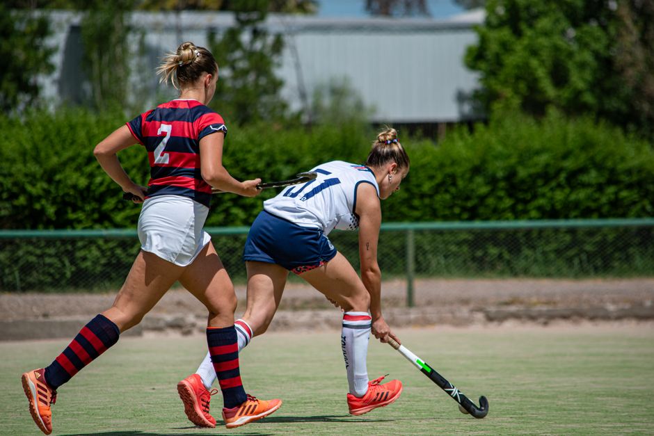 Two women play an intense field hockey game on a sunny day, showcasing skill and teamwork.