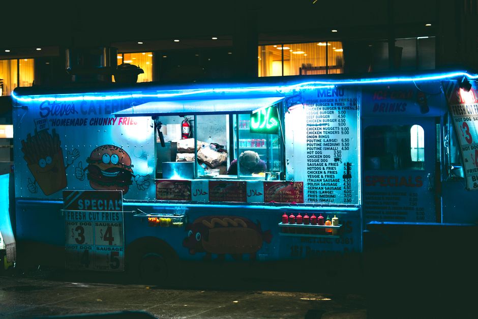 A vibrant food truck illuminated with neon lights at night, offering a variety of street f
