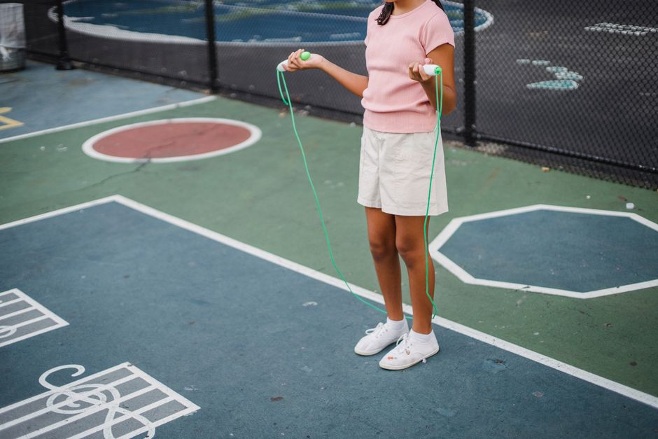 A young girl in summer attire jumping rope on a colorful outdoor court.