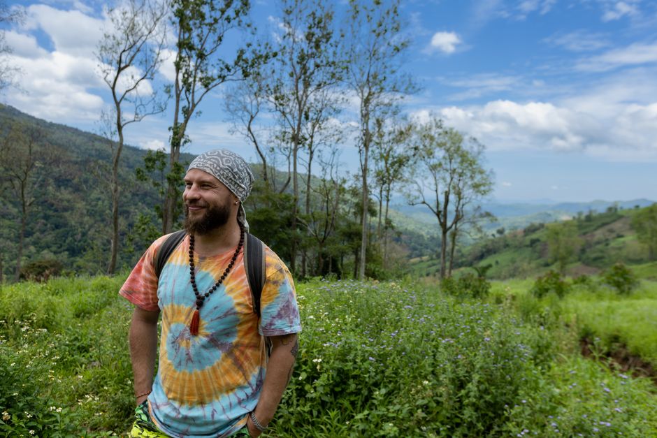 A cheery hiker in tie-dye shirt enjoying a scenic mountain meadow view.