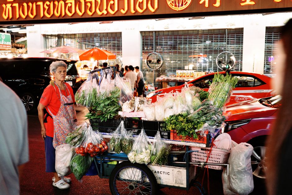 Elderly vendor selling fresh vegetables from cart at vibrant Asian night market.
