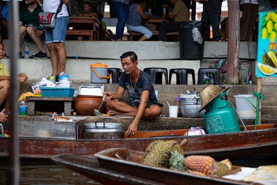 A vendor prepares food amid bustling floating market in Asia, showcasing vivid local culture.