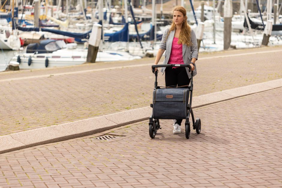 A woman pushing a baby stroller along a marina walkway with moored boats in the background.