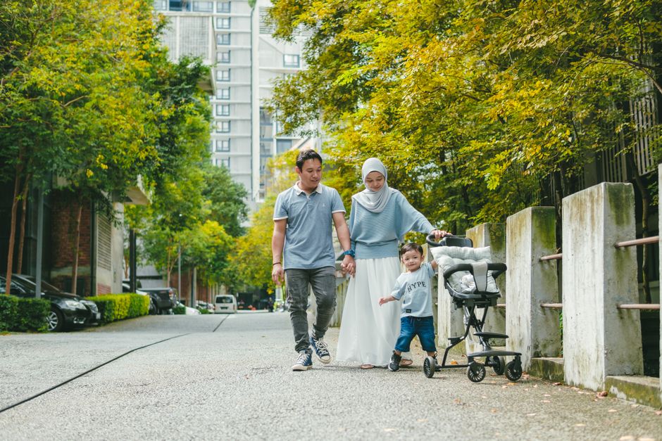 Happy family walking with a stroller in a city park, enjoying leisure time together.