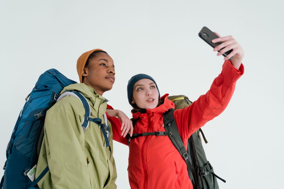 A diverse couple in jackets and backpacks taking a selfie in a studio setting, capturing their travel spirit.