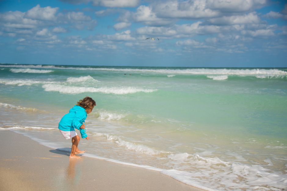 A young child plays by the ocean waves on a sunny day at the beach.