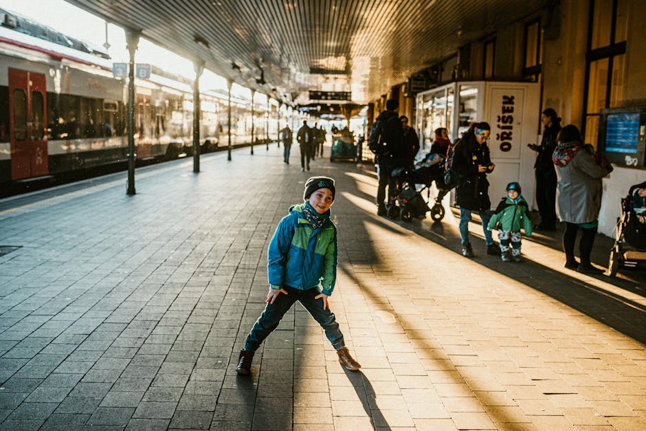 Cheerful child in winter clothing playing at a sunlit urban train station.