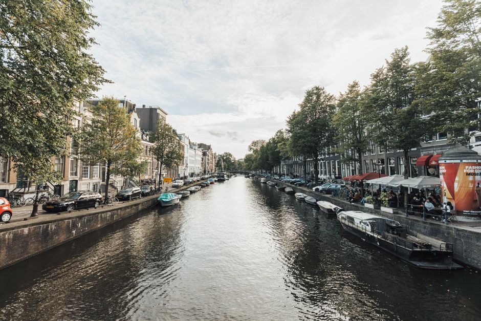 Charming view of Amsterdam's canal lined with boats, trees, and bustling cafés.