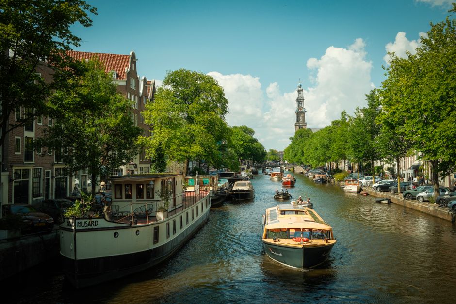 Scenic view of Amsterdam's iconic canal with historic boats and lush greenery under a bright blue sky.