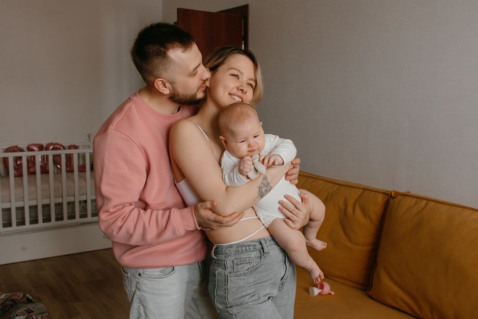 A joyful family moment with parents holding their baby in a cozy living room setting.