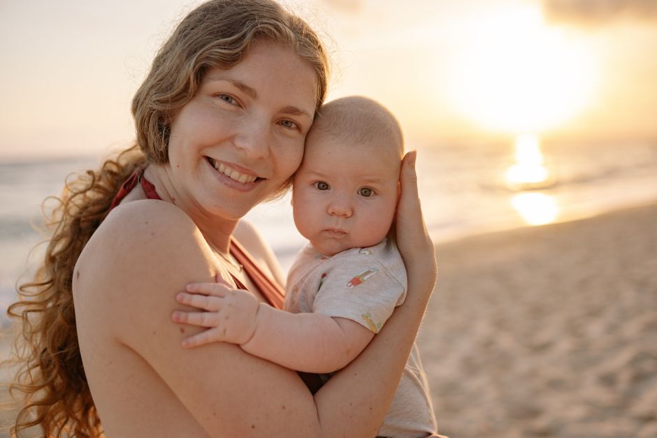 A joyful mother holding her baby on the beach during a beautiful sunset.