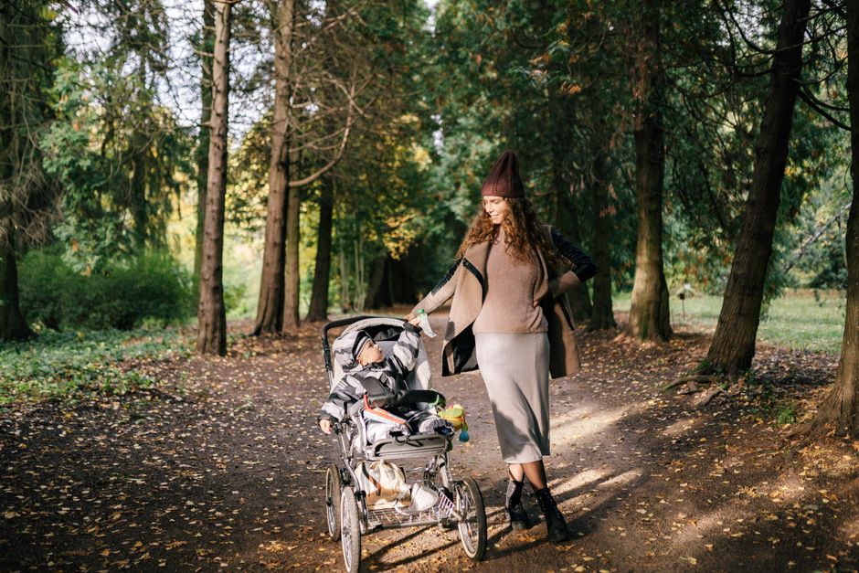 A woman with a stroller enjoys a walk in an autumn forest, surrounded by colorful trees.