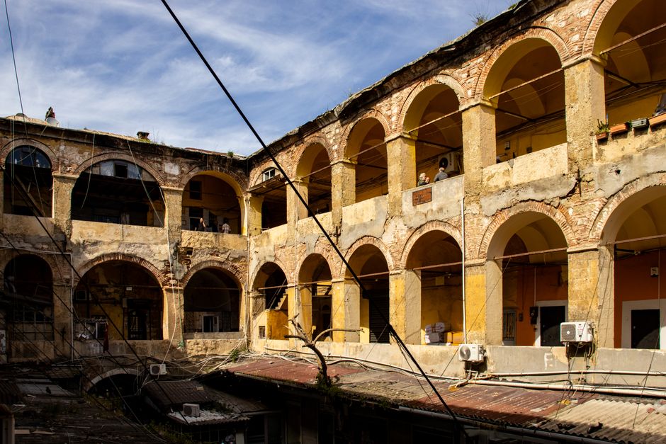 Rustic courtyard of an old abandoned building with arched architecture and sunlight casting dramatic shadows.