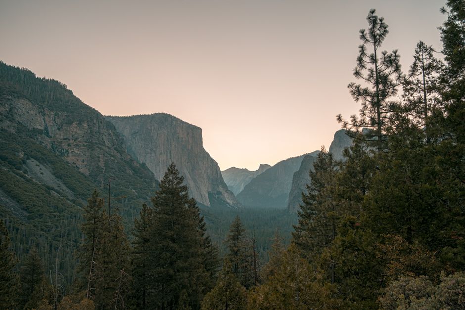 A breathtaking view of Yosemite Valley with towering cliffs and lush trees at dusk, offering a serene natural landscape.