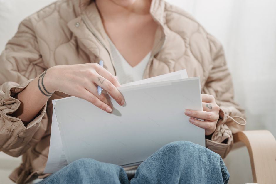 Individual in beige jacket holding and reviewing papers indoors.