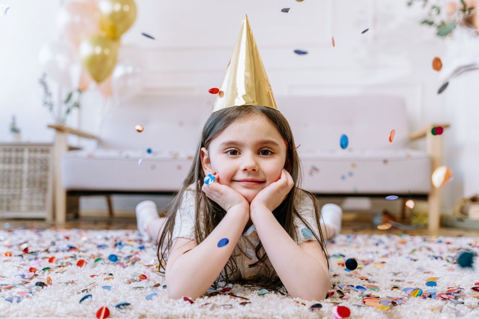 A joyful girl at a birthday party lying on the carpet surrounded by confetti.