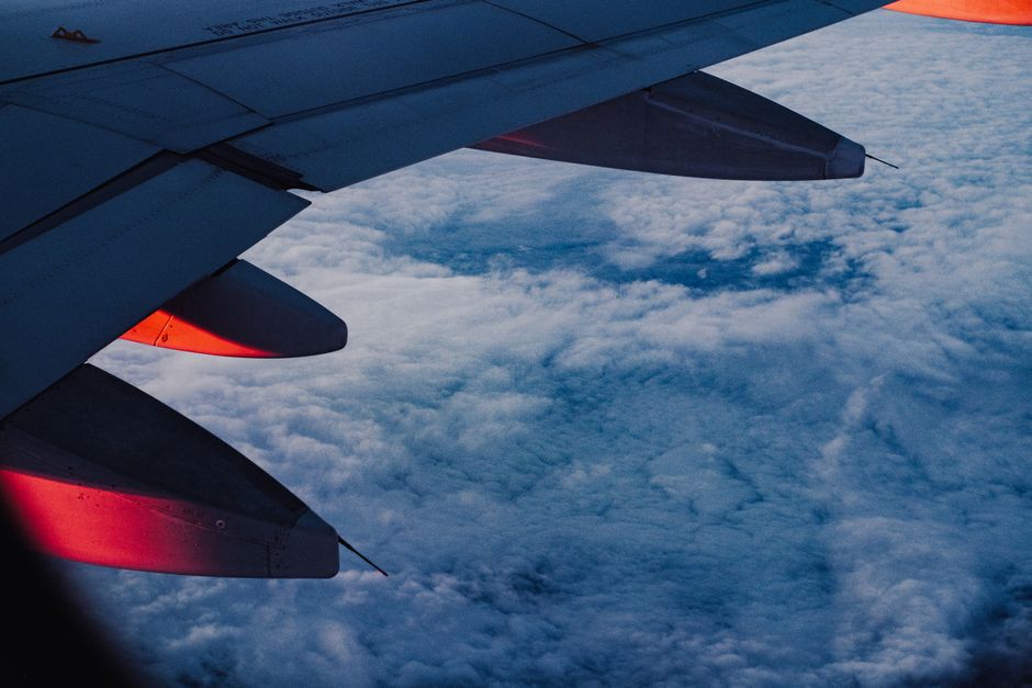 An airplane wing with dramatic lighting flying high over a sea of clouds during twilight.