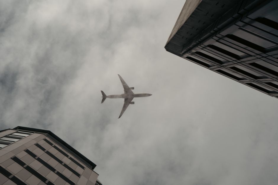 Airplane flying over skyscrapers in Tokyo, Japan, captured between city buildings on a cloudy day.