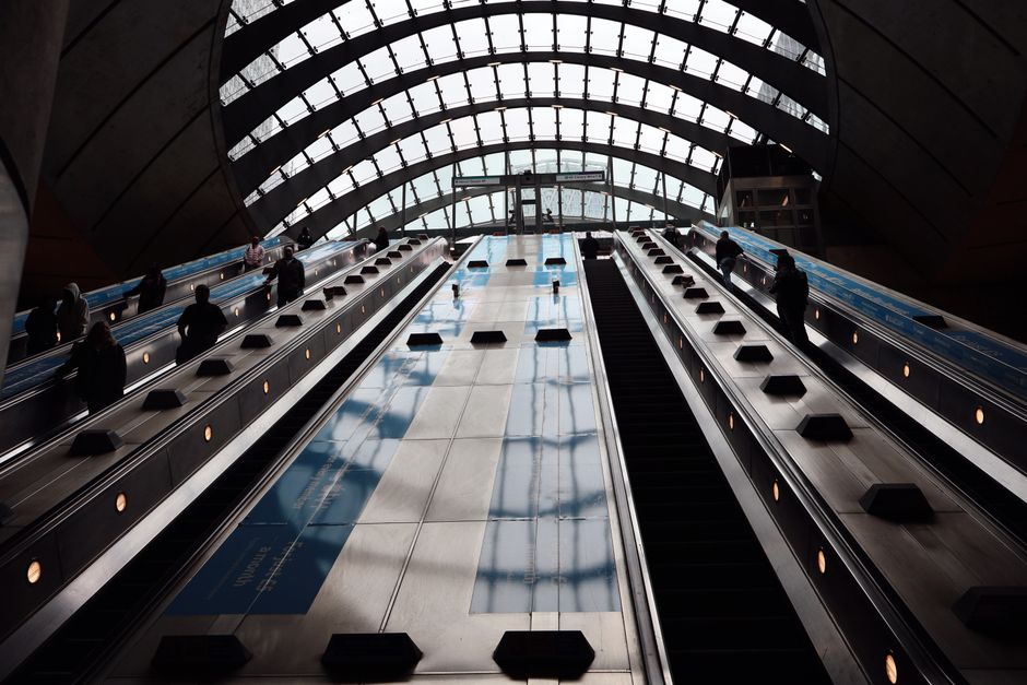 View of escalators at Canary Wharf station, London with silhouettes of people during daytime.