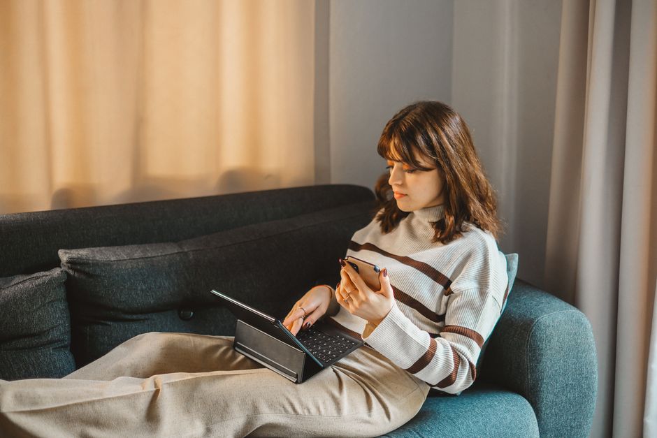 Brunette woman multitasking with tablet and smartphone on a comfortable sofa indoors.