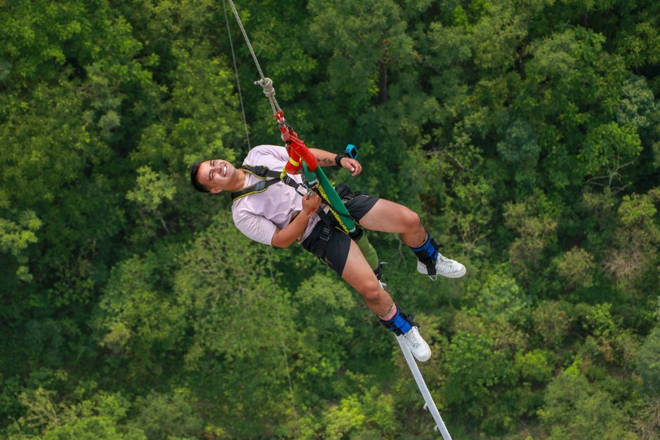 A man smiling joyfully while zip lining over a dense forest, full of adventure and excitement.