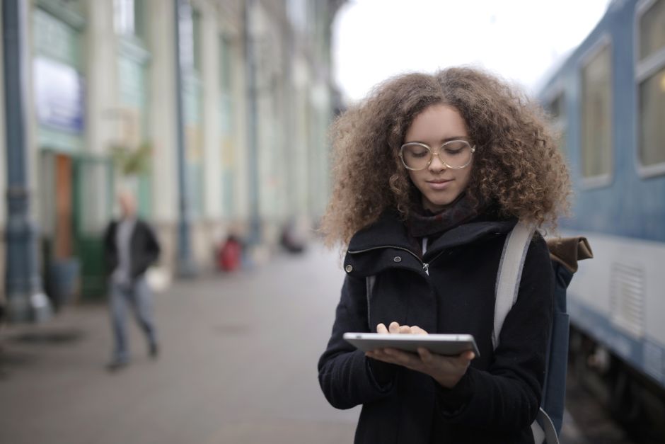 A woman standing at a train station, focused on her tablet, epitomizes the digital nomad lifestyle.