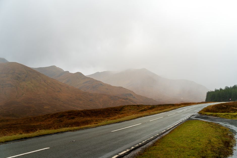 Scenic mountain road disappearing into mist with autumn colors in the highlands.