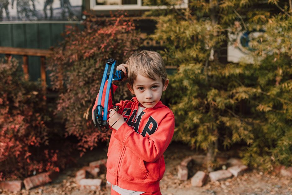 Young boy in red hoodie holding a toy bow outside during fall season.