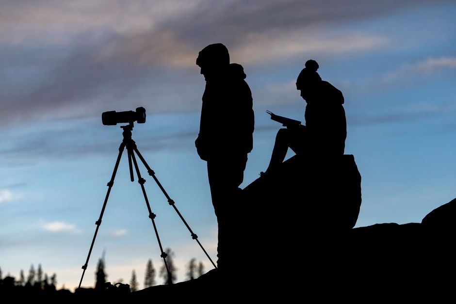 Silhouette of two photographers with camera gear under a twilight sky outdoors.