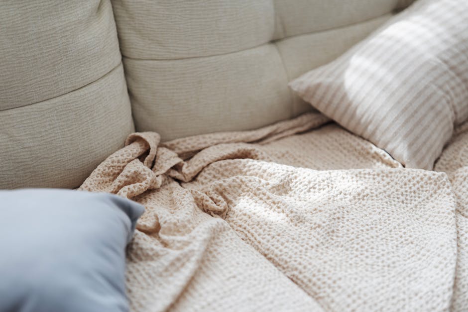 A comfortable beige couch with soft pillows and a textured blanket in a relaxed setting.