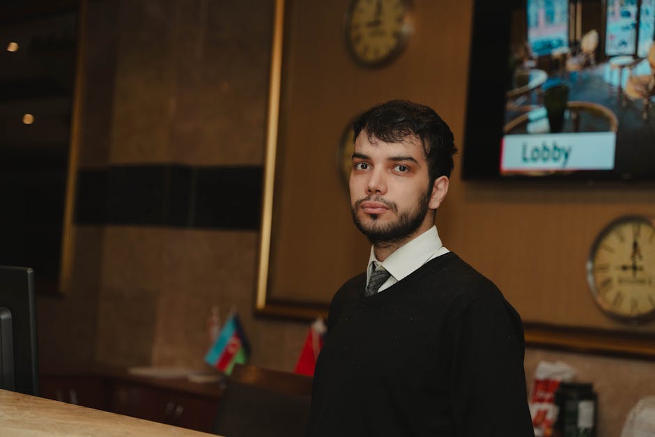 A hotel receptionist standing at the front desk in a hotel lobby, ready to assist guests.